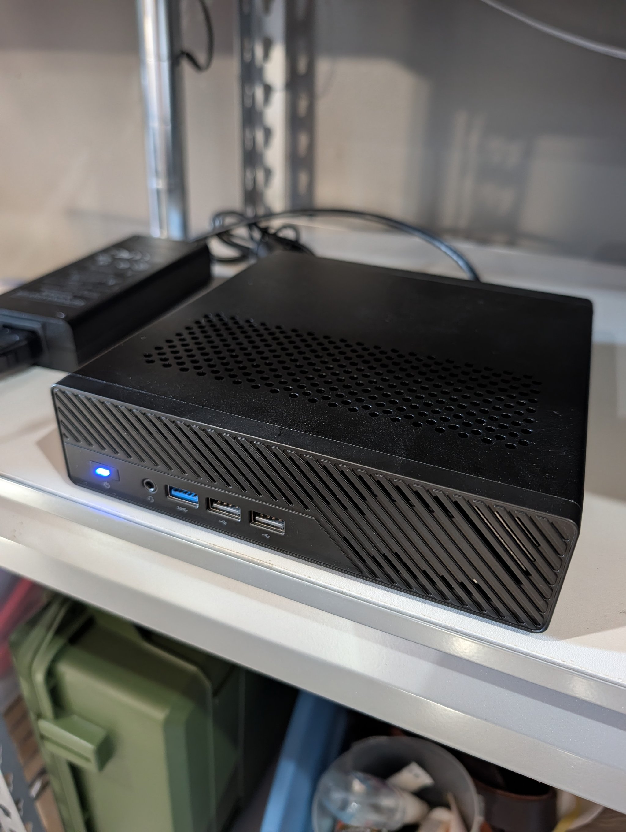 Minisforum MS-01 mini PC on a metal shelf with the blue power LED illuminated