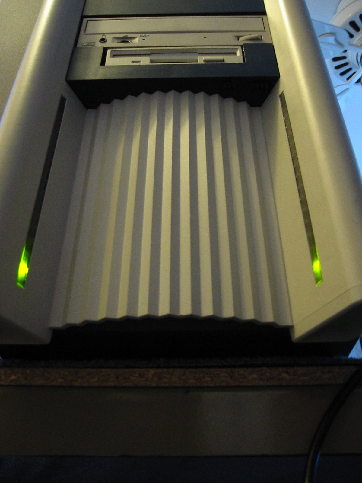 BeBox front photographed from below looking up, showing the ribbed front grille and the bottoms of the green Blinkenlights glowing in vertical slots on either side
