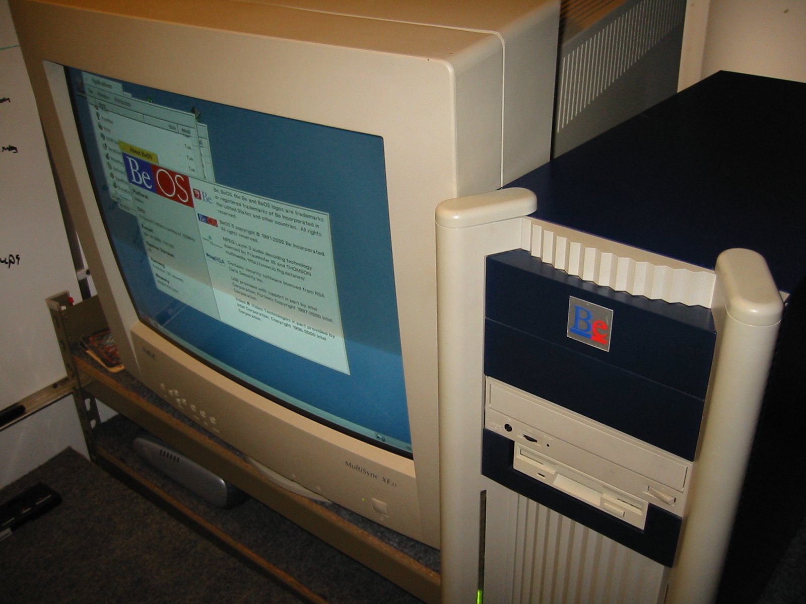 BeBox tower next to NEC MultiSync XE21 monitor showing About BeOS dialog, desk-level wide shot November 2001