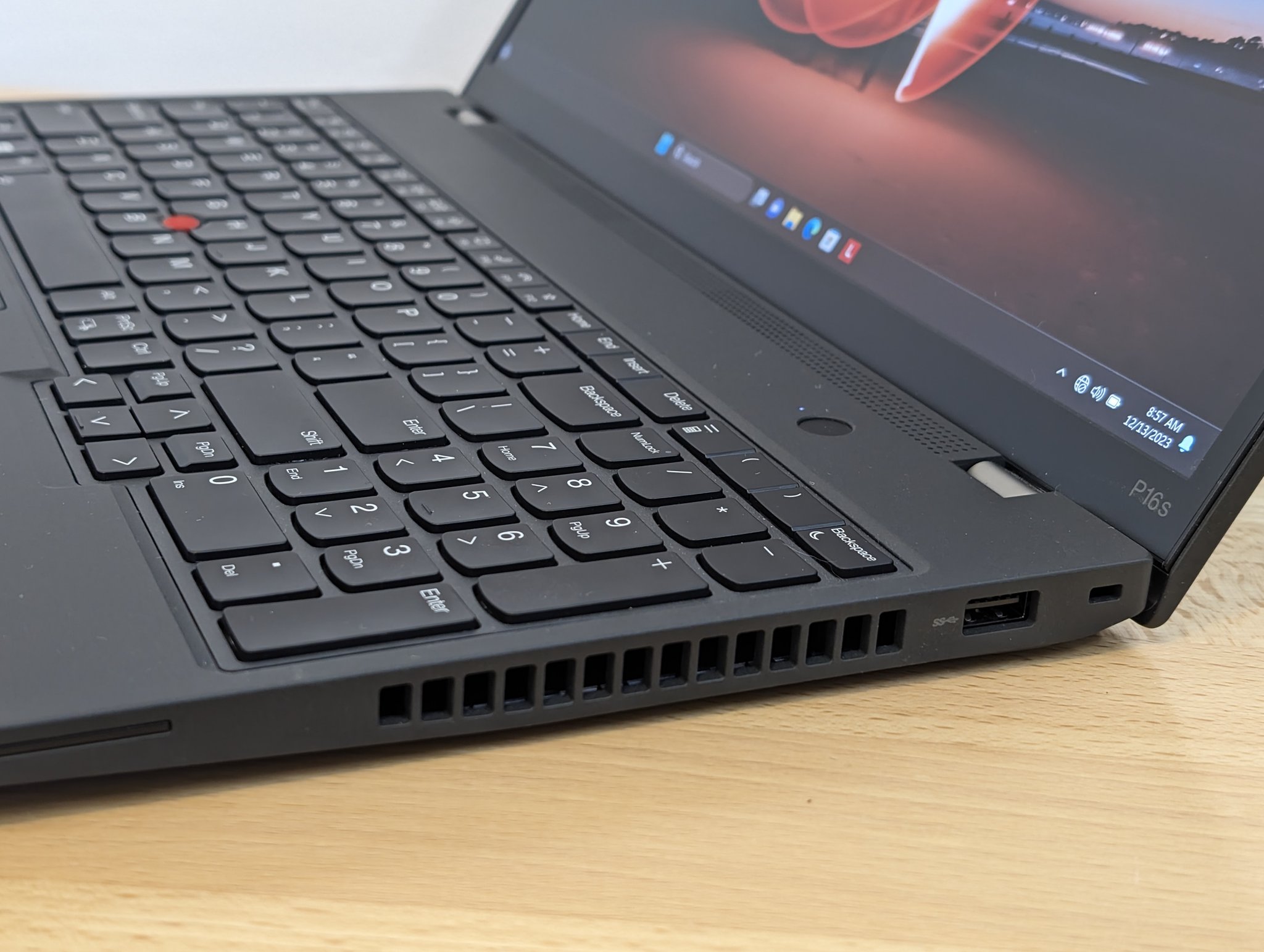 Close-up detail of the right side of a ThinkPad P16s Gen 1 keyboard, TrackPoint, ports, and right-side venting. Visible: the right half of the 6-row Precision Keyboard, the red TrackPoint nub between G, H, and B, a vent grille, a full-size USB-A port, a Kensington lock slot, and the P16s bezel label at the lower-right of the screen.