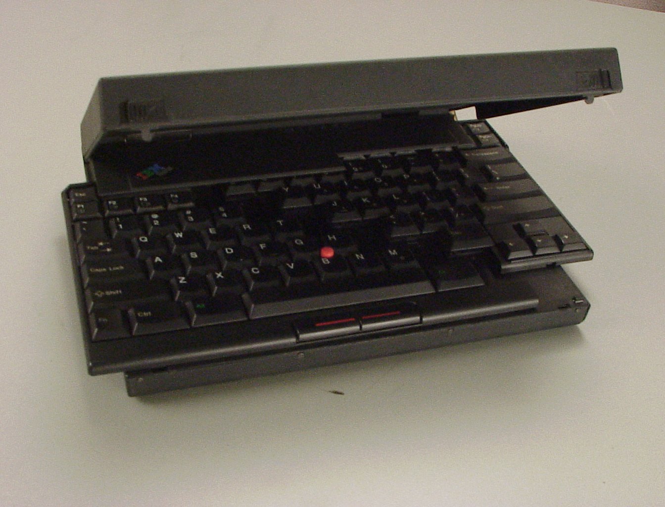 IBM ThinkPad 701 (1995) on a desk with its butterfly keyboard mechanism extended outside the chassis. The keyboard halves are wider than the laptop's closed footprint.